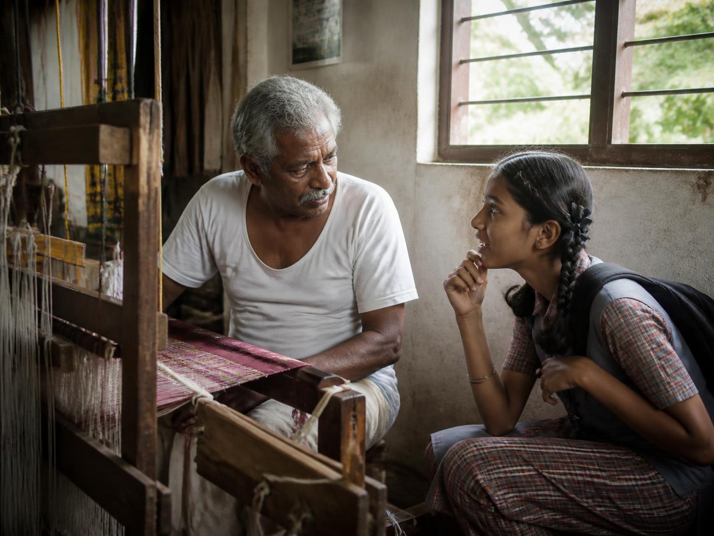 A student closely observing a handloom while talking with the weaver